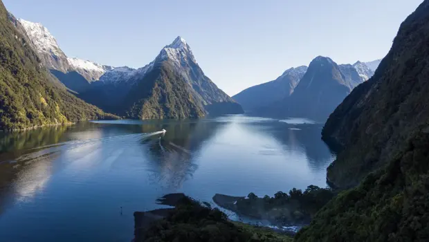 A panoramic view of Milford Sound with Mitre Peak reflecting in the water and the Milford Haven cruising through the crystal water. 