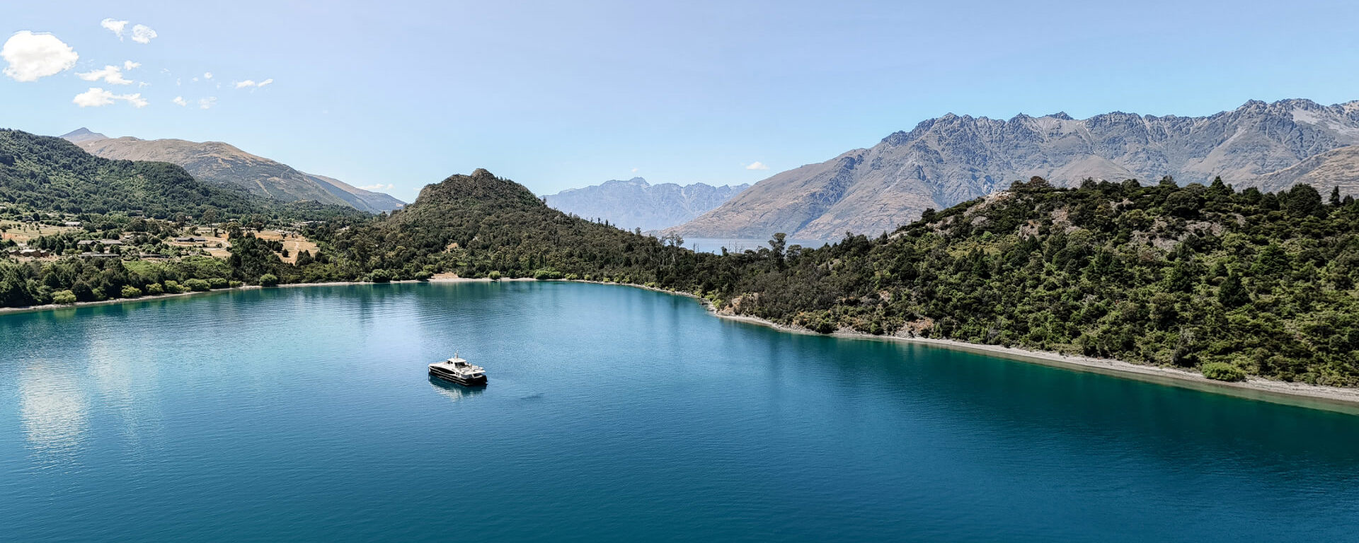 Spirit of Queenstown cruise boat floating on the calm, turquoise waters of Bob’s Cove, surrounded by lush greenery and majestic mountain views