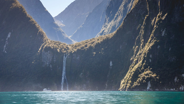 Boat in distance approaching waterfall in Milford Sound