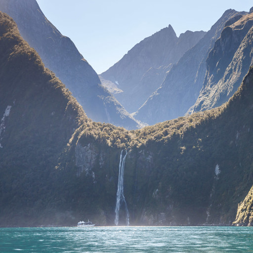 Boat in distance approaching waterfall in Milford Sound