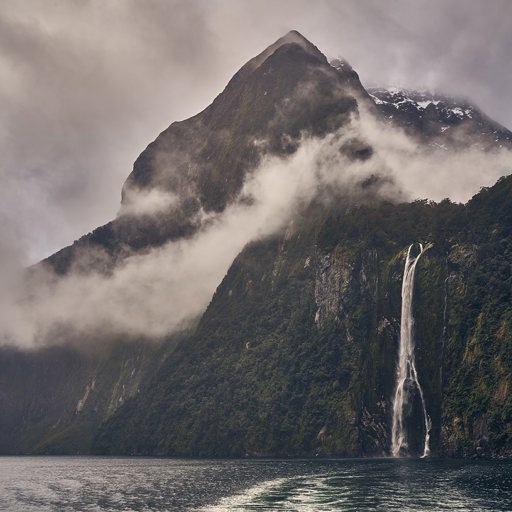 A cloudy day at Milford Sound, with a thin waterfall and mountain peaking through the clouds