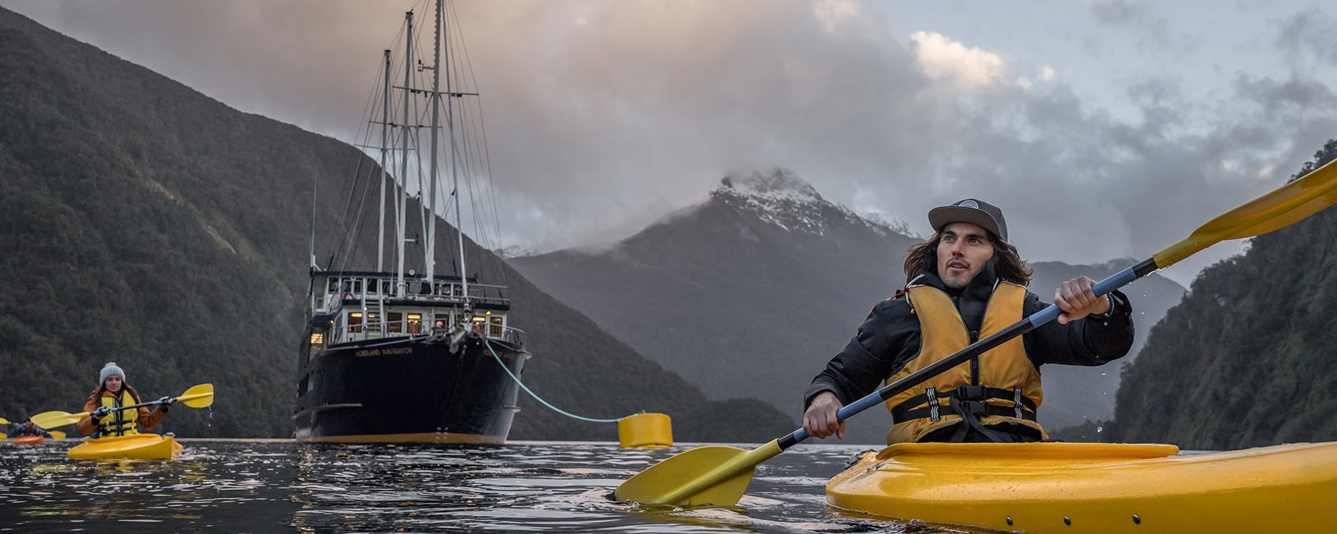 Group of kayakers in Doubtful Sound with boat and mountains in the background