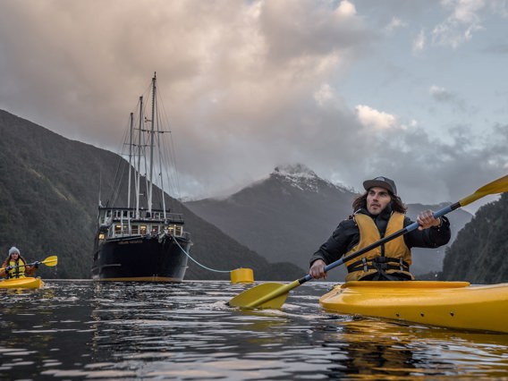 Group of kayakers in Doubtful Sound with boat and mountains in the background