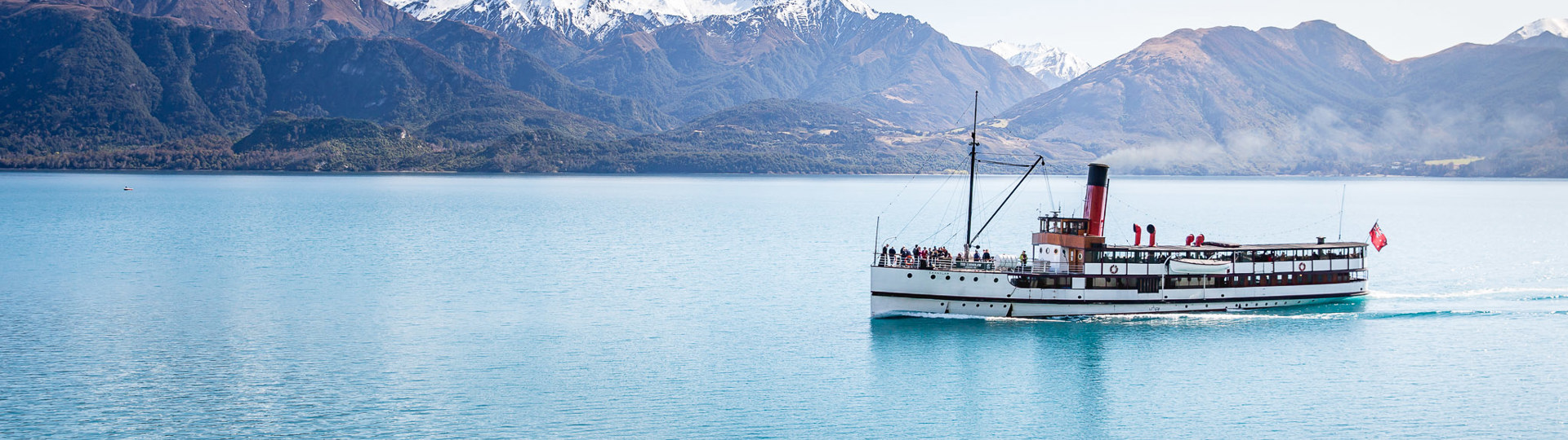 The historic TSS Earnslaw Steamship cruises along Lake Wakatipu with a view of The Remarkables mountain range 