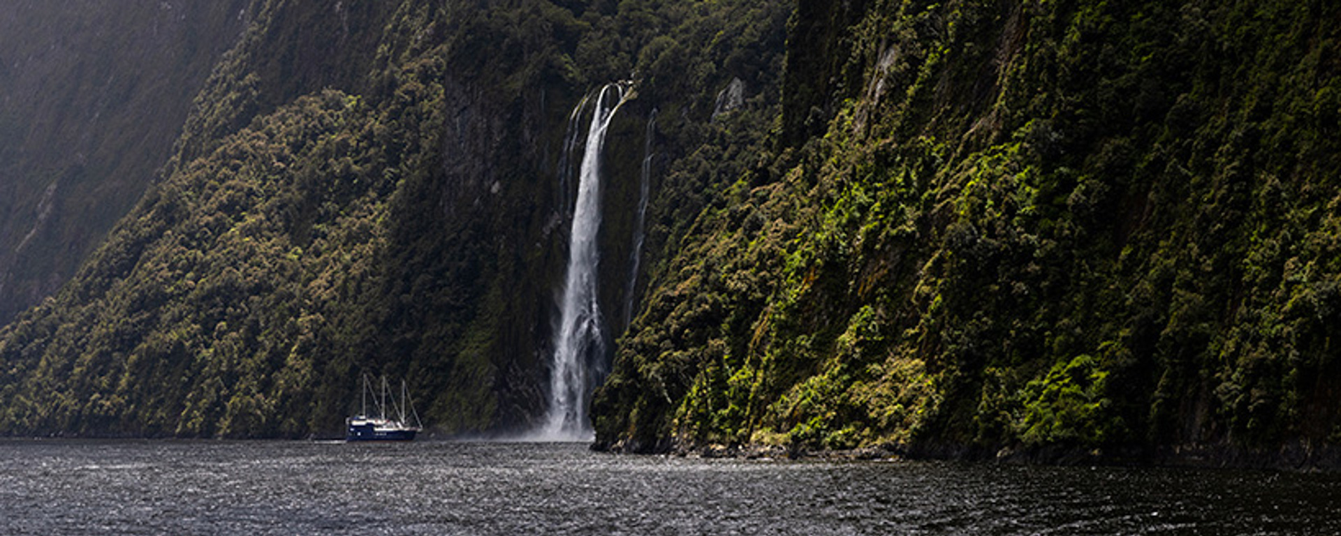 The Milford Mariner vessel cruises close to a cascading waterfall in Milford Sound