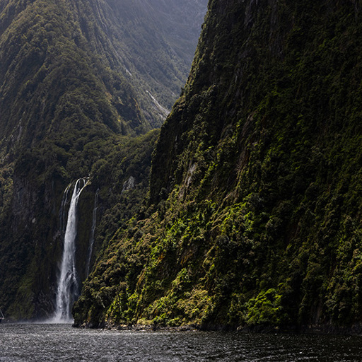 The Milford Mariner vessel cruises close to a cascading waterfall in Milford Sound