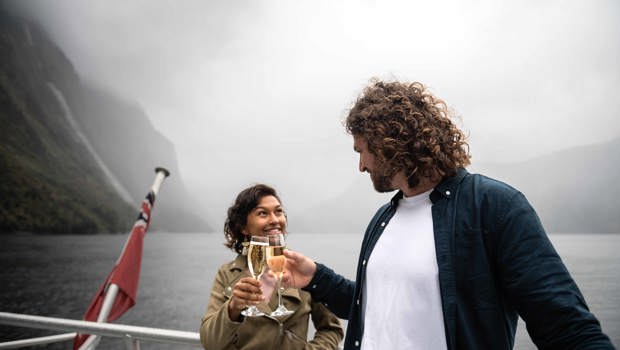 A couple cheers a glass of champaign on board the premium cruise in Milford Sound