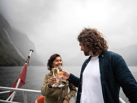 A couple cheers a glass of champaign on board the premium cruise in Milford Sound