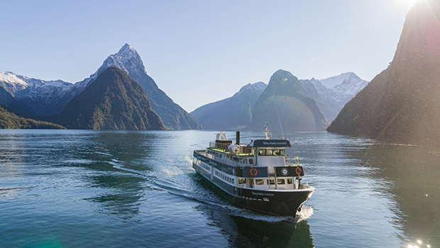 The Milford Haven vessel cruises through Milford Sound on a clear day, with a snowy Mitre Peak in the background 