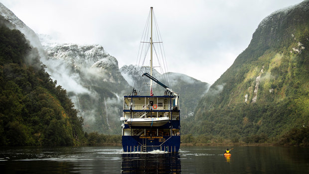 The Fiordland Navigator vessel cruises in a peaceful Doubtful Sound, alongside a kayaker