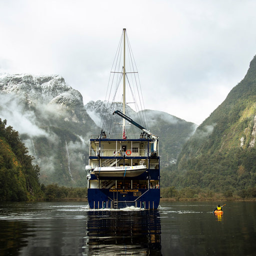 The Fiordland Navigator vessel cruises in a peaceful Doubtful Sound, alongside a kayaker