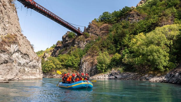 A rafting group float under the Kawarau bridge on a clear blue day 