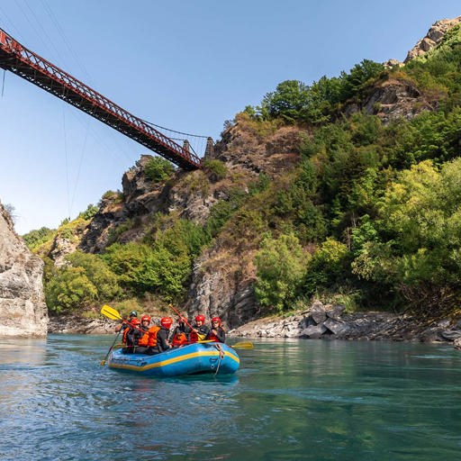 A rafting group float under the Kawarau bridge on a clear blue day 