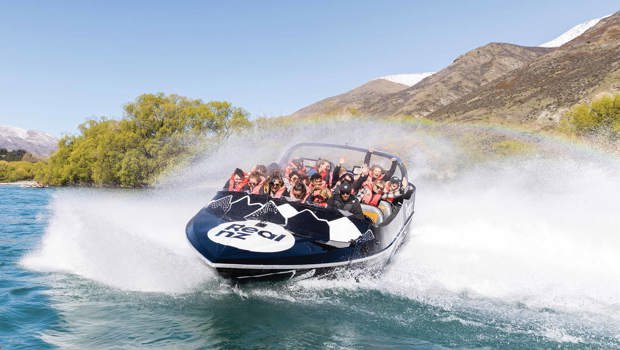 An excited crowd enjoy a 360 spin in the Queenstown Jet Boat, encompassed by a rainbow