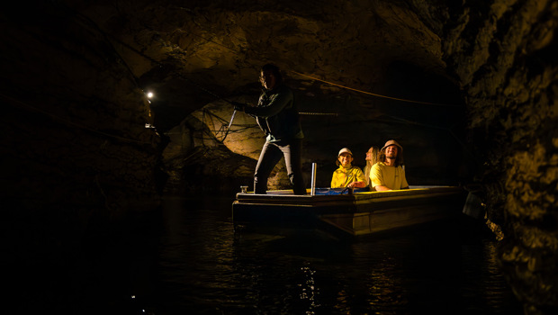 A group of three are guided through an underground cave on a small boat 