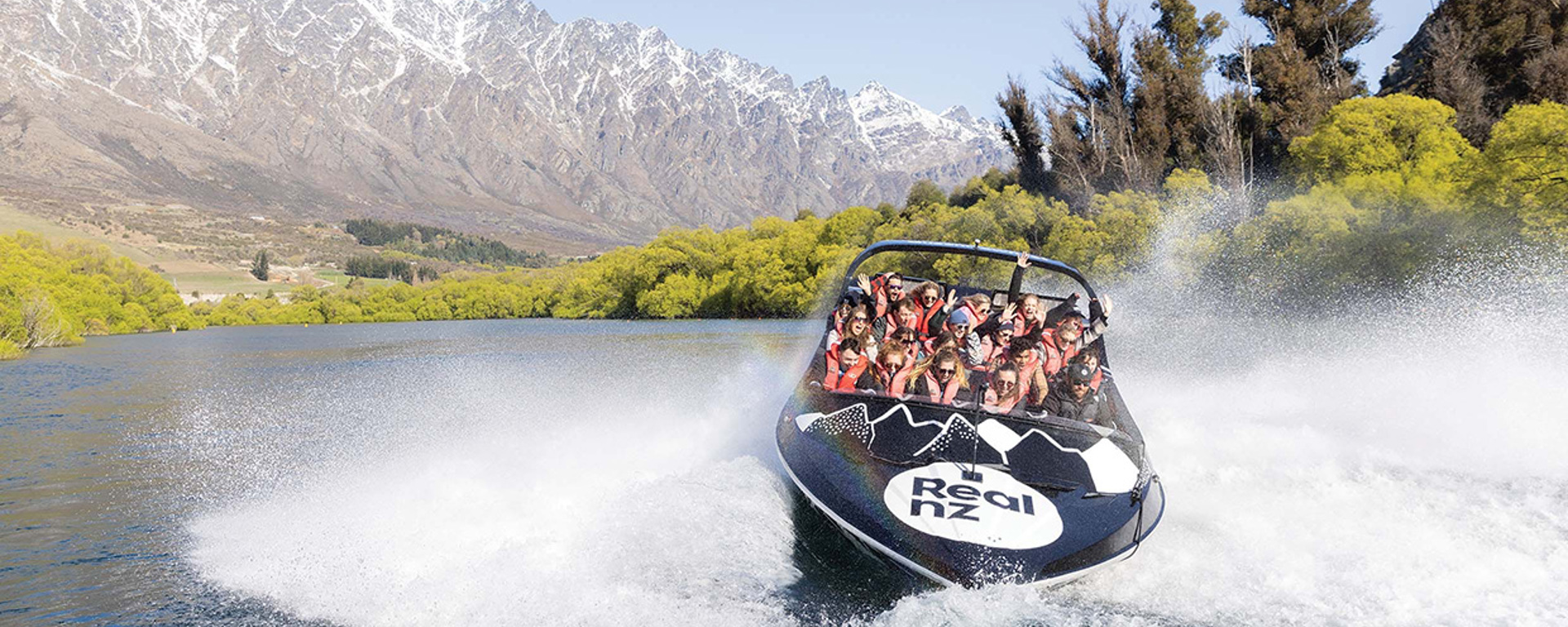 An excited crowd enjoy a 360 spin in the Queenstown Jet Boat in front of the Remarkables mountain range