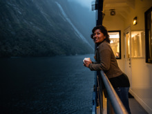 A woman leans over the edge of the vessel while cruising in Milford Sound at dusk