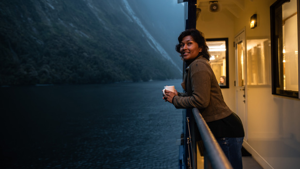 A woman leans over the edge of the vessel while cruising in Milford Sound at dusk