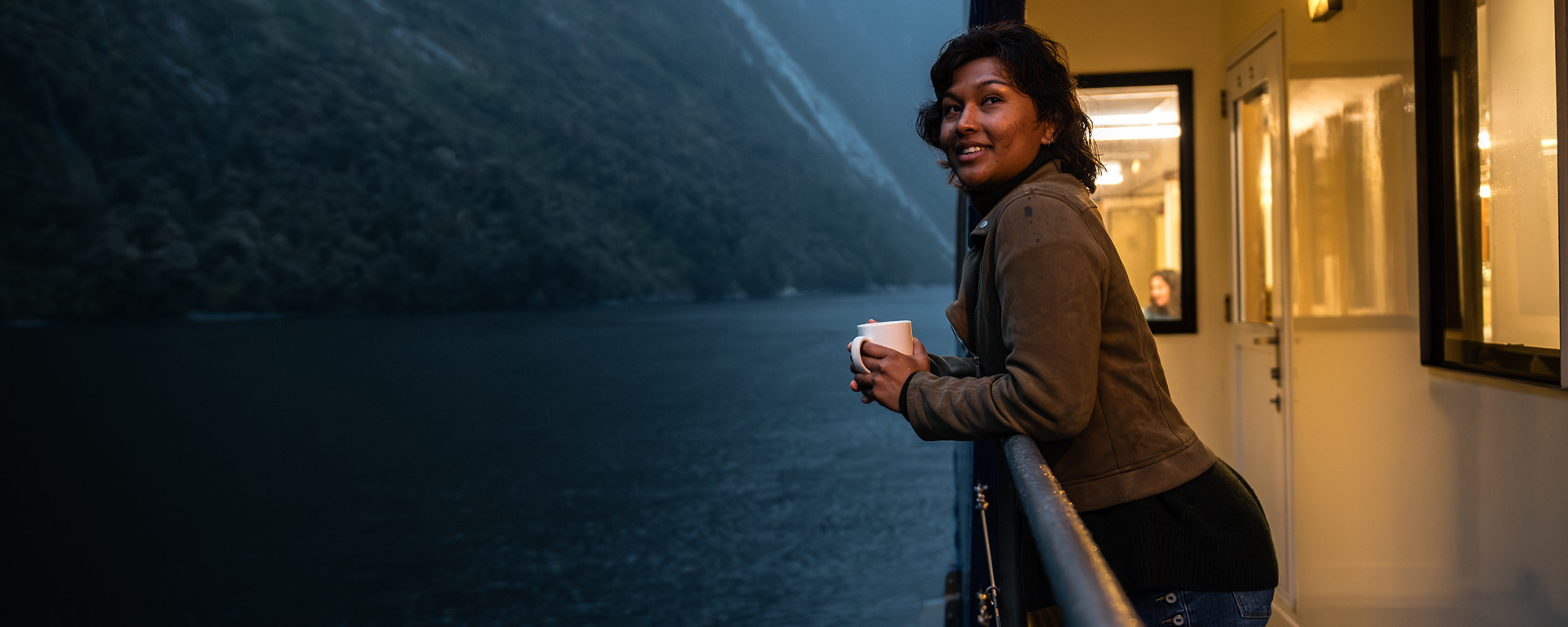 A woman leans over the edge of the vessel while cruising in Milford Sound at dusk