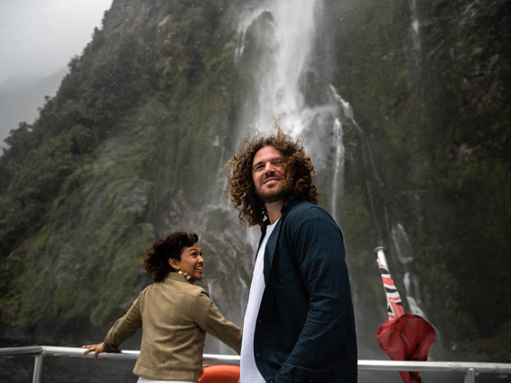 A couple enjoy being up close to a waterfall while cruising n Milford Sound