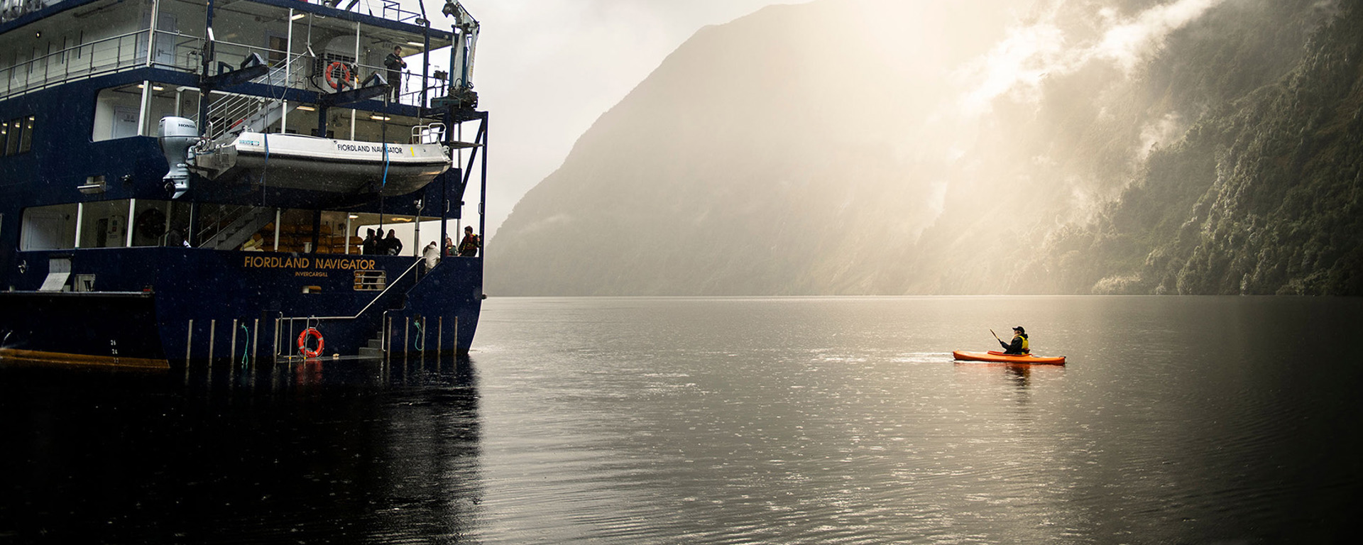 A kayaker floats near the Fiordland Navigator vessel on the water at Doubtful Sound