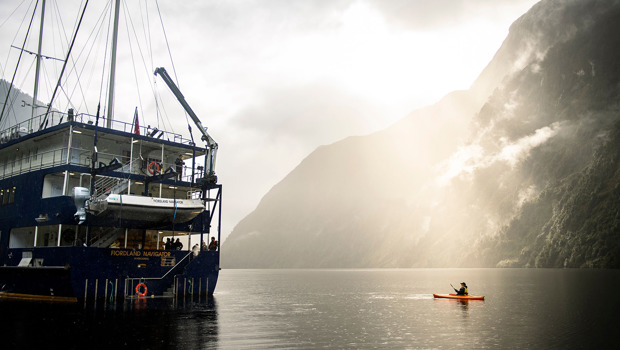 A kayaker floats near the Fiordland Navigator vessel on the water at Doubtful Sound