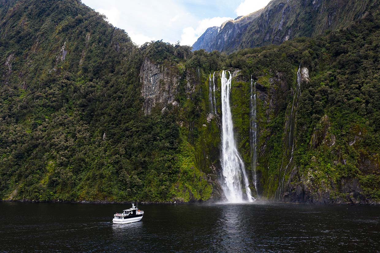 Wide shot of The Sovereign vessel cruising in front of a waterfall on Milford Sound