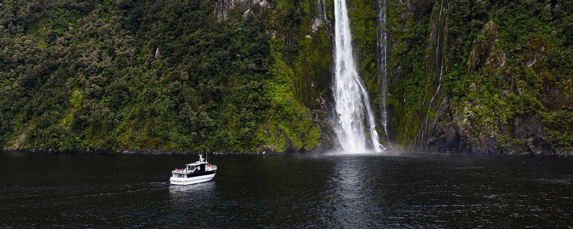 Wide shot of The Sovereign vessel cruising in front of a waterfall on Milford Sound