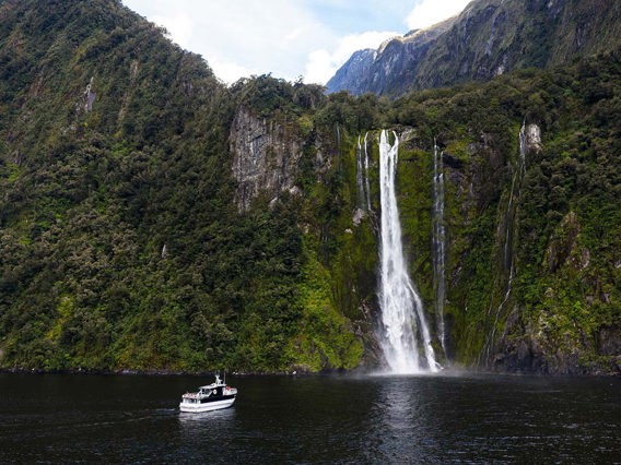 Wide shot of The Sovereign vessel cruising in front of a waterfall on Milford Sound