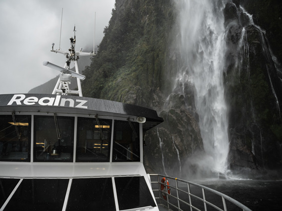 A close shot of The Sovereign vessel cruising under a waterfall in Milford Sound