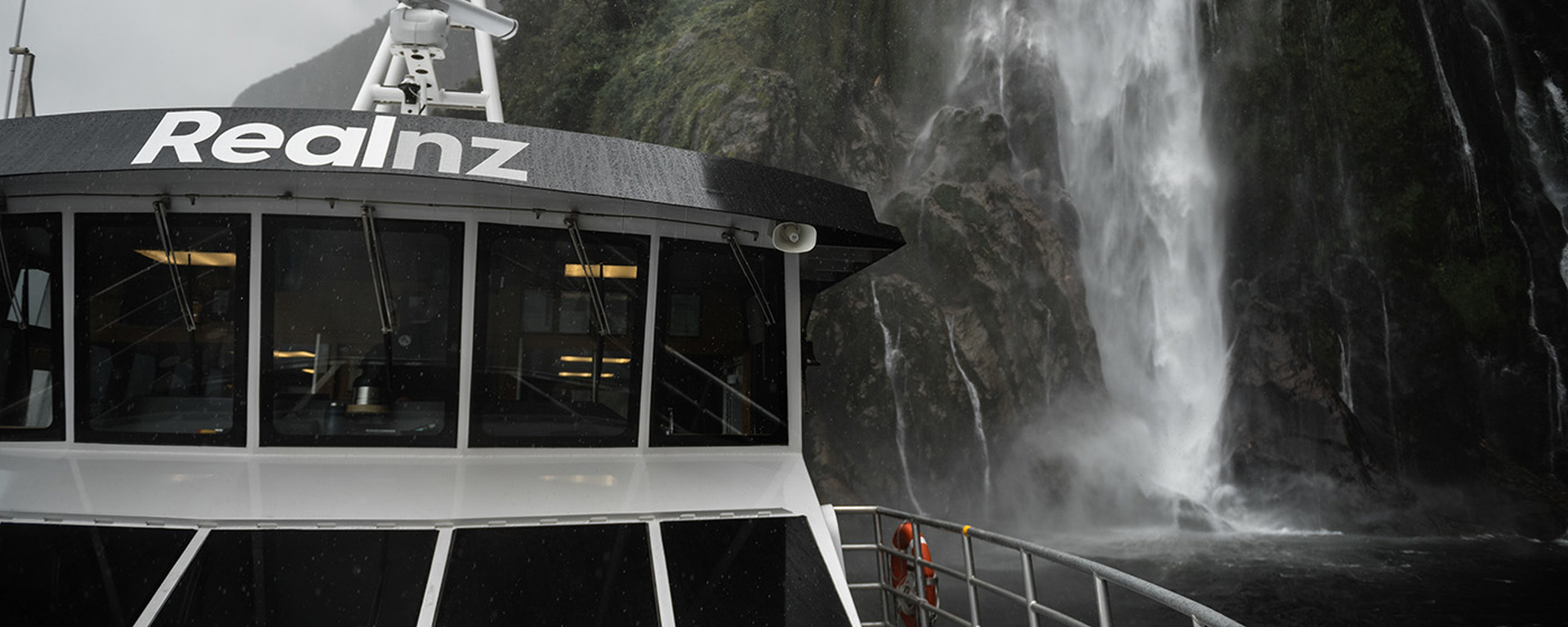 A close shot of The Sovereign vessel cruising under a waterfall in Milford Sound