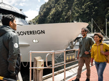 A couple walk along the wharf at Milford Sound and are greeted by a crew member before their cruise