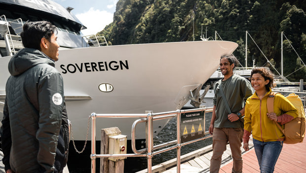 A couple walk along the wharf at Milford Sound and are greeted by a crew member before their cruise