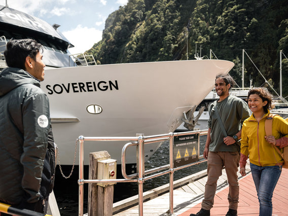 A couple walk along the wharf at Milford Sound and are greeted by a crew member before their cruise