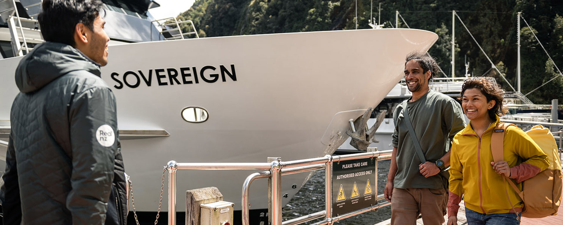 A couple walk along the wharf at Milford Sound and are greeted by a crew member before their cruise