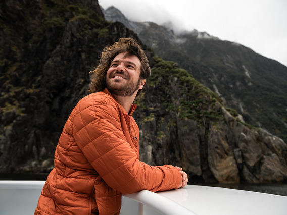 A man enjoys the view from the top deck of a vessel while cruising Milford Sound