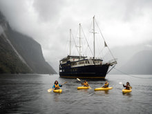 A group of four kayakers floating on Milford Sound in front of the Milford Wanderer vessel