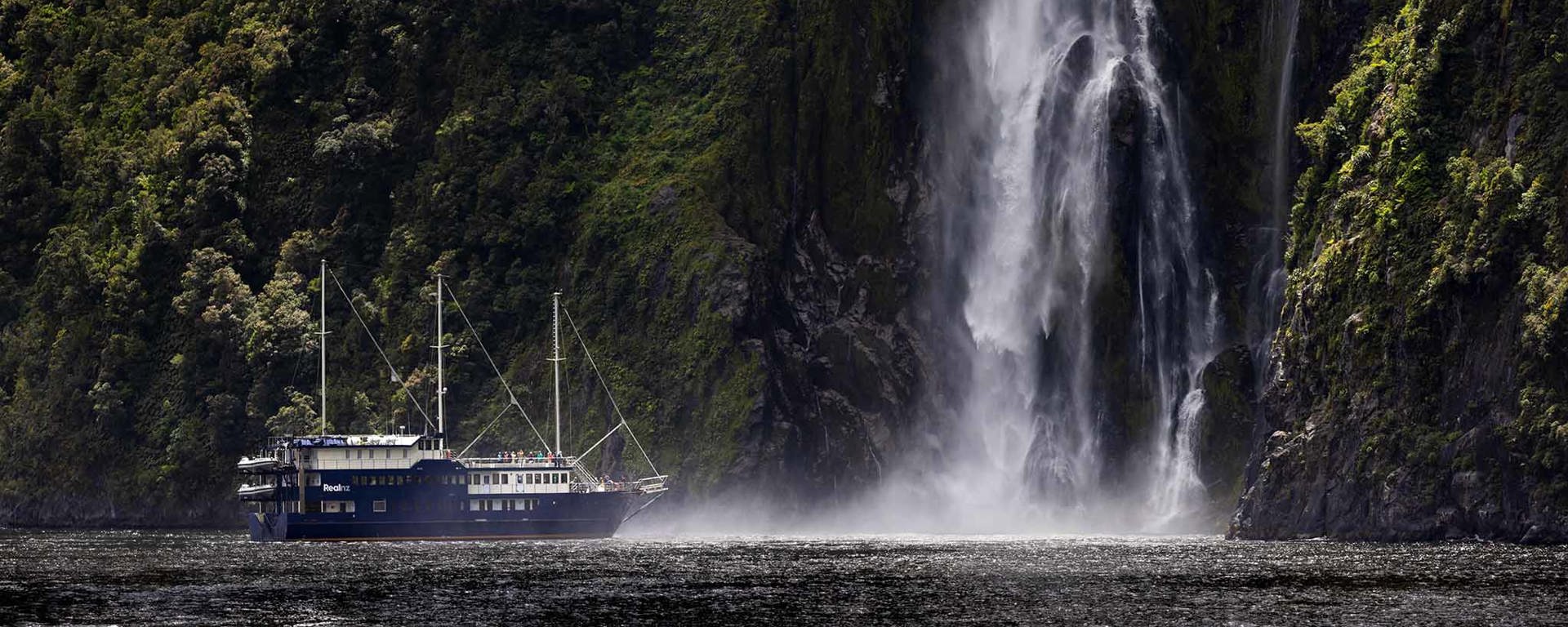 The Milford Mariner vessel cruises close to a cascading waterfall in Milford Sound