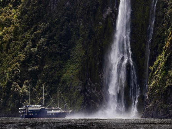 The Milford Mariner vessel cruises close to a cascading waterfall in Milford Sound