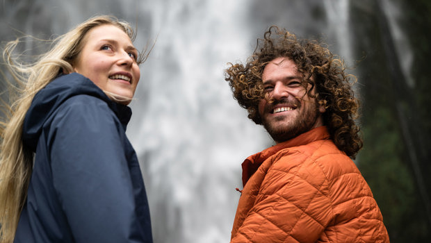 A couple look back over their shoulder with a cascading waterfall behind them