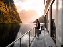 A man stands on the side deck of a vessel cruising through Doubtful  Sound at golden hour