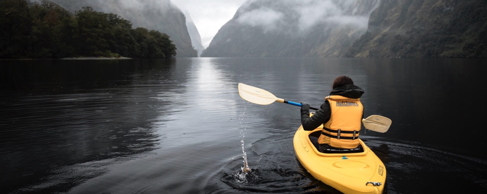 A bright yellow kayak floats along the water in gloomy Doubtful Sound 