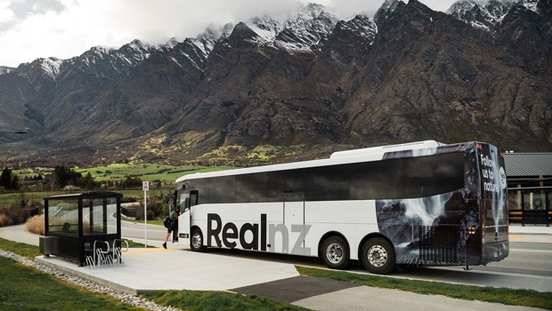 A RealNZ branded coach stops at the bottom of the snowy Remarkables mountain range