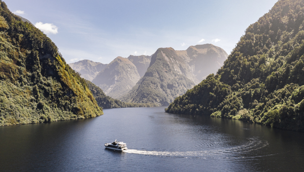 Wide shot of a motorised vessel cruising through Doubtful Sound on a bluebird day