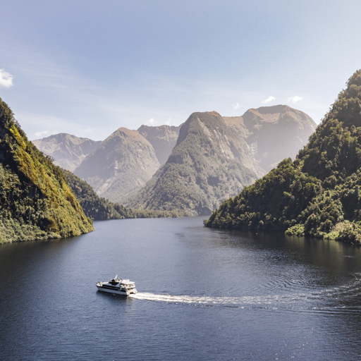 Wide shot of a motorised vessel cruising through Doubtful Sound on a bluebird day