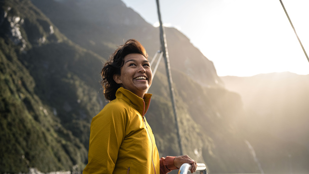 A woman in a bright yellow jacket enjoys the view of sunny Doubtful Sound from the top deck of a vessel