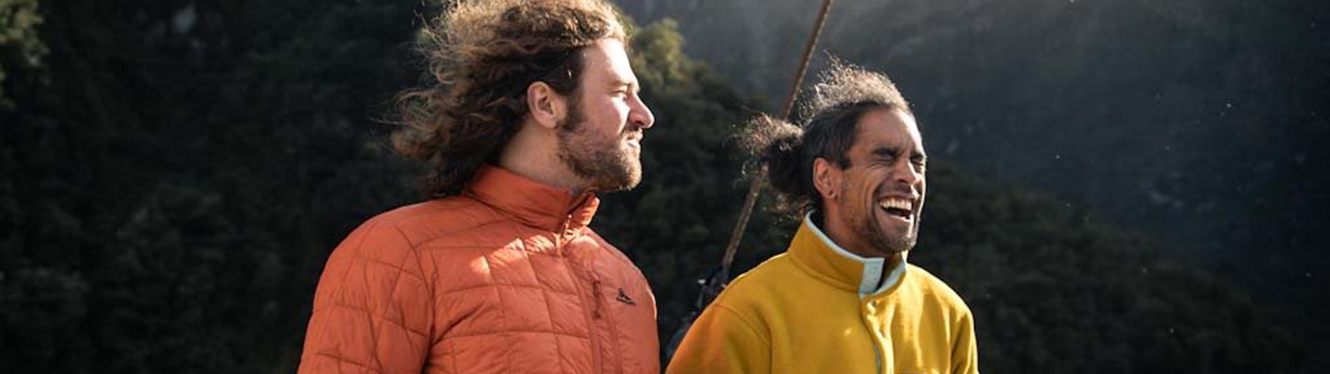 Two men enjoy a hot drink on the outside deck onboard a cruise on Doubtful Sound