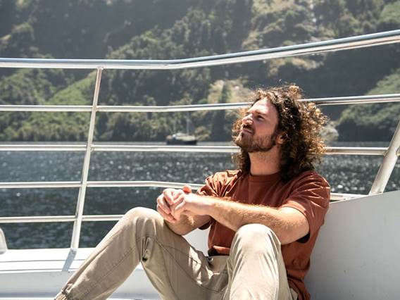 A man enjoys the sunshine while sitting outside on a cruise of Doubtful Sound 