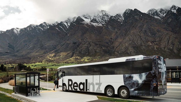 A man getting on the Real NZ coach in front of the Remarkables mountain range