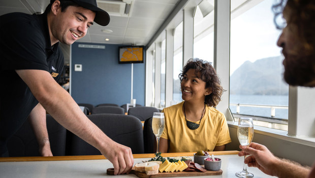 A staff member delivers a cheese platter to guests on a Milford Sound cruise.